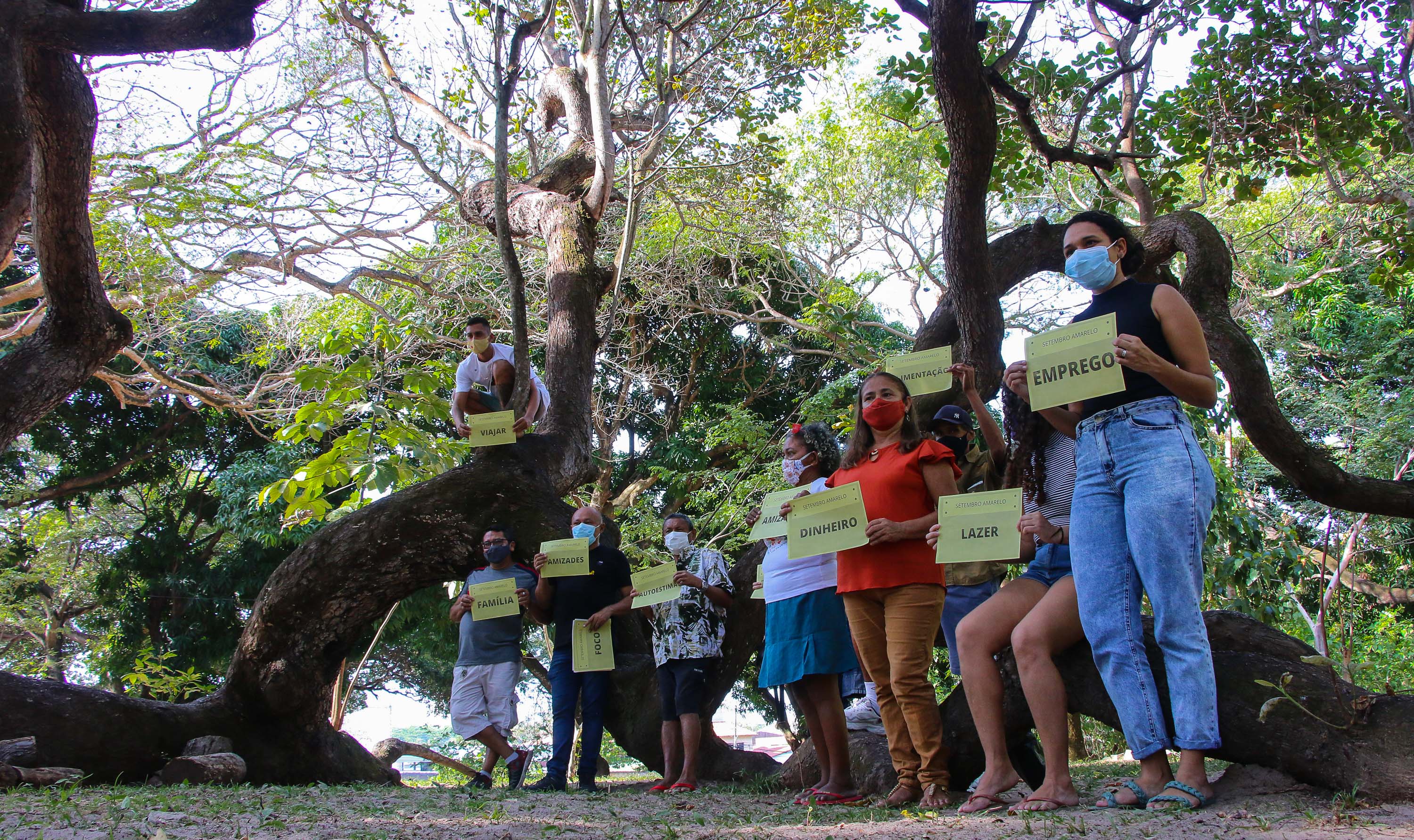 um grupo de pessoas com máscara posa numa área verde na casa josé de alencar, eles seguram cartazes com palavras de auto-afirmação, como vida, saúde e emprego